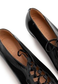 Ballerine in vernice nera con design allacciato e dettagli traforati. Texture liscia e soletta marrone chiaro con logo.