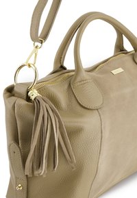 Beżowa skórzana torba o teksturowanej powierzchni, z podwójnymi uchwytami, odczepianym paskiem na ramię, złotymi detalami oraz dekoracyjnym frędzlem.