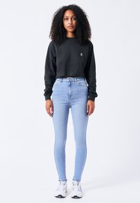 Sudadera negra corta con mangas largas y un pequeño logo; jeans ajustados de talle alto en azul claro; zapatillas blancas con detalles en gris.