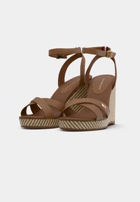 Sandales compensées marron avec une bride de cheville, présentant des bandes croisées à l'avant, une plateforme tissée texturée et un accent rayé sur la bride arrière.