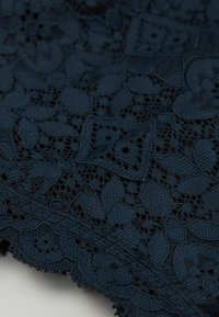 Donkerblauwe kant stof met ingewikkelde bloemmotieven, vierkante patronen en gegolfde randen. De textuur is delicaat en open op bepaalde plaatsen.