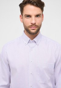 Witte blouse met knopen, voorzien van een rood-blauw geruit patroon, klassieke kraag en een borstzak met kleine knoopdetails.