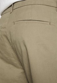 Spodnie khaki o delikatnej fakturze, z tylną kieszenią i prostym krojem. Materiał wydaje się wytrzymały, z czystym, gładkim wykończeniem.