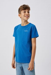 T-shirt en coton bleu à manches courtes avec un logo blanc "T.W.S.N." sur le côté gauche. Texture douce ; design à col rond.