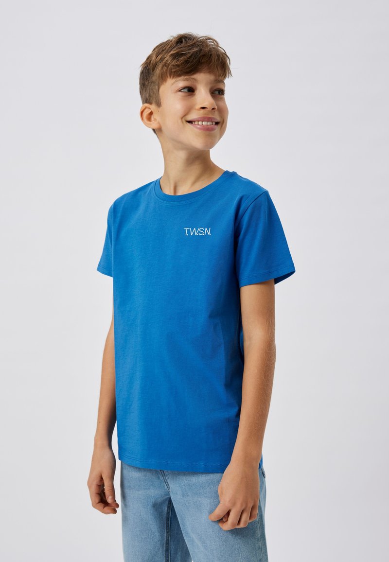T-shirt en coton bleu à manches courtes avec un logo blanc "T.W.S.N." sur le côté gauche. Texture douce ; design à col rond.