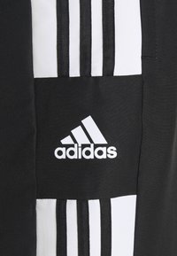 Sort atletisk stof med et hvidt Adidas-logo. Tre lodrette hvide striber krydser en solid sort sektion til venstre.