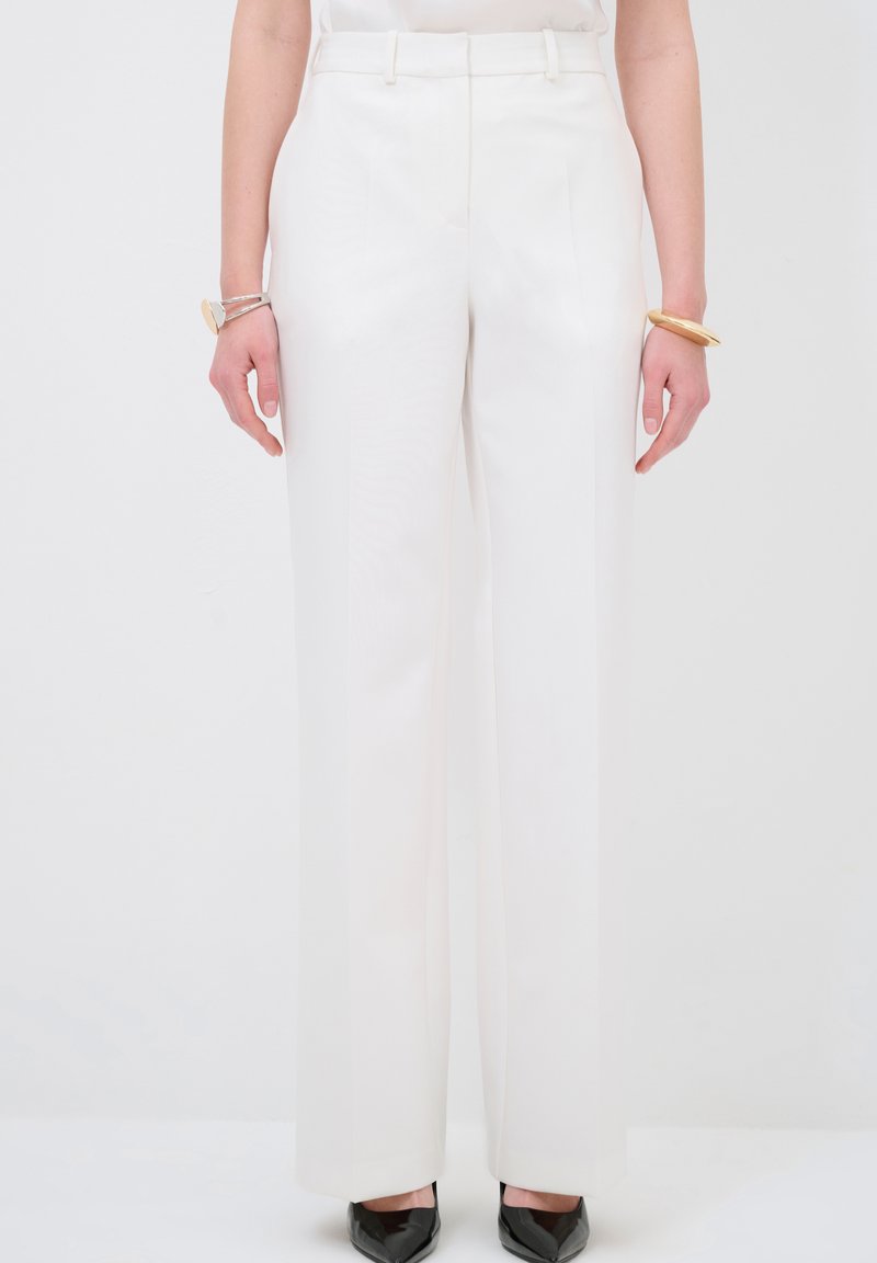 Witte op maat gemaakte broek in een soepele stof, met een hoge taille en wijde pijpen. Gecombineerd met zwarte puntige schoenen.