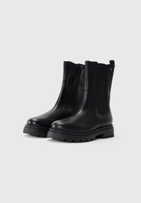 Bottes noires en cuir à chevilles avec un bout rond, fermeture éclair sur le côté, panneaux élastiques et une semelle épaisse et robuste. Dispose d'une languette à l'arrière.