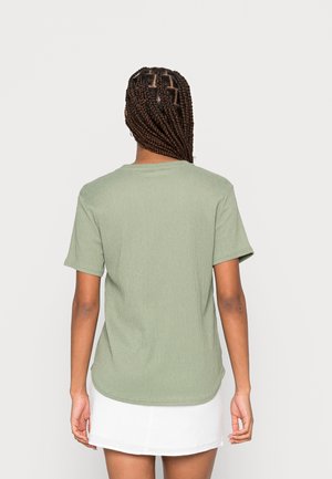 Oliivinvihreä lyhythihainen t-paita, jossa on teksturoidusta kankaasta valmistettu materiaali, pyöreä kaula-aukko ja hieman kaartuva helma.