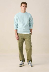 Sweatshirt bleu clair avec des poignets et un ourlet côtelés, associé à un pantalon tapered vert olive et des sneakers grises avec des accents bleus.