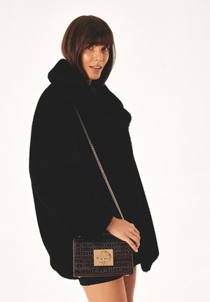 Cape en fausse fourrure noire avec un col montant, associée à un sac à main en cuir texturé marron avec un fermoir en or et une bandoulière en chaîne.