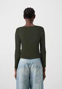 Mørkegrønn ribbet langermet topp med vid utringing, kombinert med lyseblå høytlivsjeans med to baklommer og en avslappet passform.