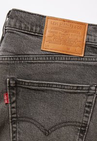 Poche arrière d'un jean Levi's noir avec un patch de marque en cuir et une étiquette en tissu rouge Levi's sur la couture de la poche.