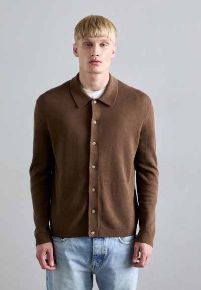 Brown cardigan sweater with a soft texture, collar, and gold buttons, worn over a white T-shirt and paired with light blue jeans.