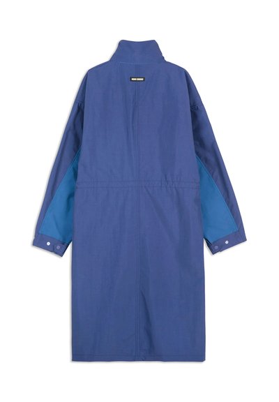 Long blue coat featuring a high collar, buttoned cuffs, and contrasting blue side panels. Made of smooth fabric with a simple design.