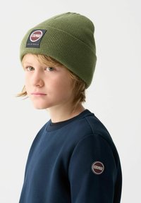 Zelená pletená čapica s rebrovanou textúrou a logom našitým na povrchu; námornícky sveter so zaobleným výstrihom a logom na rukáve.