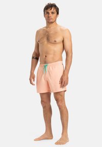 Shorts de bain pêche avec une taille élastique et un cordon turquoise. Fabriqués en tissu léger, présentant un design uni.