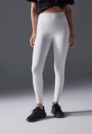 White leggings made of stretchy fabric with a high waistband, paired with black athletic shoes. Smooth texture and fitted design.