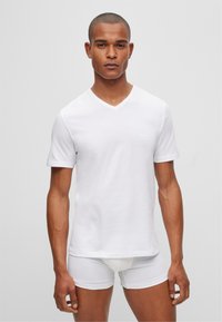 White cotton V-neck t-shirt with short sleeves, featuring a subtle logo on the chest, paired with white fitted shorts. Smooth texture.