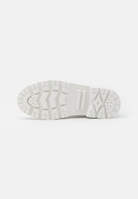 Suela de zapatilla blanca con tacos profundos, que presenta un patrón texturizado y acentos elevados para mayor agarre. Sección de entresuela lisa con agujeros de ventilación.