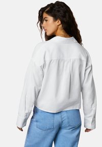 Bela kratka majica z dolgimi rokavi, manšetami z gumbi in zadnjo gubo, v kombinaciji z svetlo modrimi visokim pasom kavbojkami.