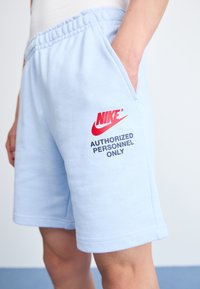Lyseblå bomulds shorts med elastisk talje, sidelommer og rødt Nike-logo med teksten "BARE AUTORISERET PERSONALE" i sort.