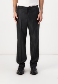 Pantalones de rayas negras con un corte relajado, que cuentan con una cintura con cuerda y un detalle de marca sutil, fabricados con una tela suave.