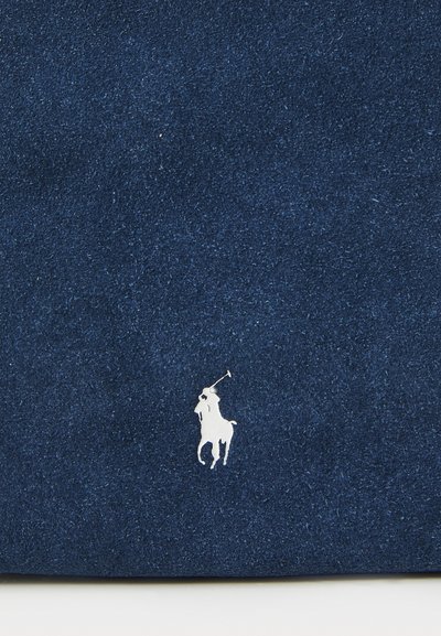 Navy zilas audums ar baltu polo spēlētāja logo, kas novietots apakšējā kreisajā stūrī.