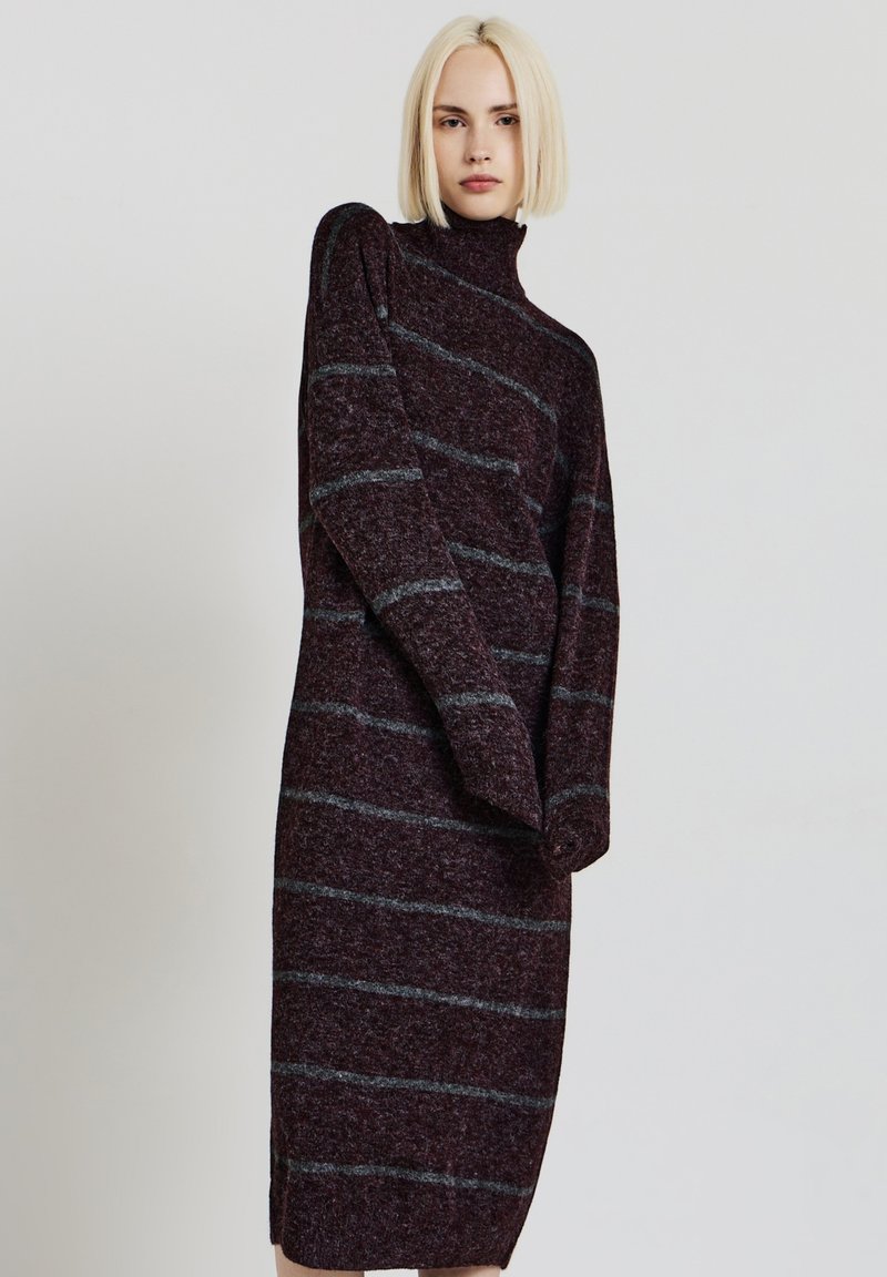 Abito a maglia bordeaux con strisce grigie, collo alto e maniche lunghe. Presenta un design snello e spacchi laterali per facilitare i movimenti.