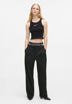 Czarny prążkowany crop top z logo, zestawiony z czarnymi spodniami z wysokim stanem i plisami oraz paskiem z denimu. Dopasowany krój, gładka tekstura.