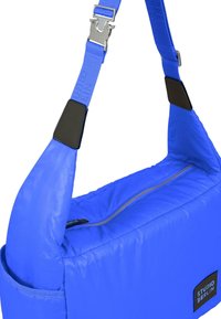 Borsa a spalla in nylon blu con texture imbottita, zip diagonale e patch con logo. Cinghia regolabile e dettagli in metallo.
