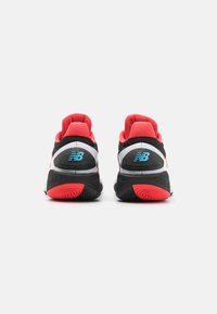 Crne i crvene atletske cipele, s podstavljenim okvirom, bijelim detaljima i teksturiranom crnom potplatu s crvenim ukrasima. Vidljiv New Balance logo.