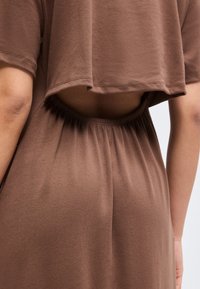 Κοντινό πλάνο ενός ατόμου που φοράει καφέ ρούχα με κοντό τοπ που αποκαλύπτει ένα άνοιγμα στο μέσο της πλάτης και ελαστική ζώνη μέσης με ψηλή μέση.