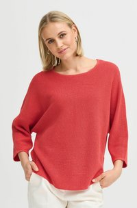 Pull tricot à côtes rouges avec un large col, des manches trois-quarts et une coupe décontractée, associé à un pantalon crème.