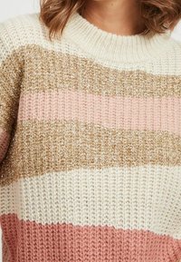 Neulottu paita, jossa vaakasuorat raidat väreissä kerma, kulta, vaaleanpunainen ja koralli. Kassan koholla oleva neulos ja resorikaulus.