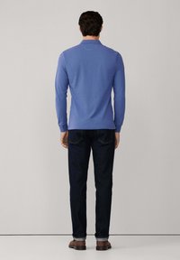 Camisa polo azul de manga larga con cuello, combinada con jeans de denim oscuro. El conjunto presenta un corte clásico y un diseño sencillo.