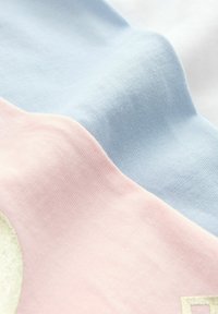 Tessuto di cotone diviso in tre sezioni orizzontali: rosa pallido, azzurro chiaro e bianco. Superficie texturizzata con una leggera rigatura e un accento beige lungo il bordo.