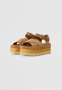 Sandalias de plataforma de ante marrón con una gruesa suela intermedia de yute trenzado y una suela de goma ligera; cuenta con una correa ajustable en el tobillo y un diseño de punta abierta.