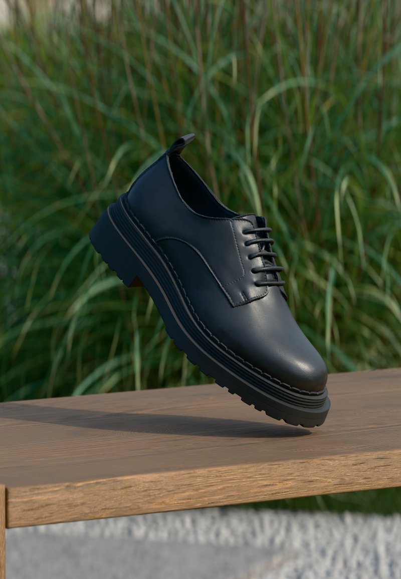 Μαύρο δερμάτινο παπούτσι δετό με χοντρή σόλα που αιωρείται πάνω από ξύλινο παγκάκι, φόντο με πράσινο γρασίδι.