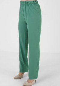 Vihreät, joustavyötäröiset housut, joissa on löysä istuvuus ja suorahihnainen muotoilu. Kangas on sileä, ja housut on yhdistetty vaaleanbeigeihin korkokenkiin.