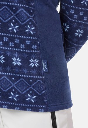 Fleece sweater in navy with light blue snowflake and geometric patterns. Features a side tag and soft texture. Zipper details visible.