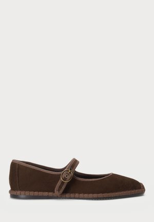 Zapato plano de ante marrón con punta redonda, una correa tipo Mary Jane con una hebilla circular de latón y una suela de textura trenzada.