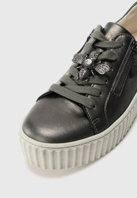Metallisk grå lærersneaker med texturert grå snøring, glidelås og en dekorativ bieaccent på overdelen. Tykk såle med hvite striper.