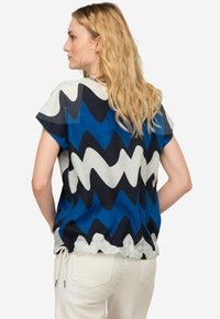 Top maniche corte con un motivo a zigzag nei toni del blu, nero e bianco. Il tessuto è morbido, con un dettaglio a laccio all'orlo.