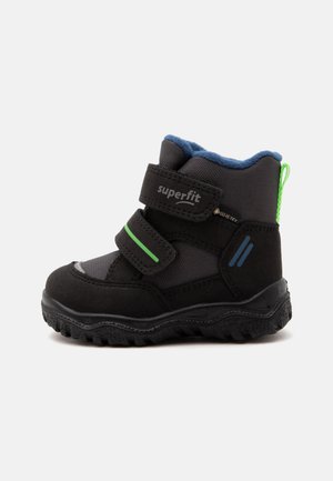 Μαύρη παιδική χειμερινή μπότα με λουράκια Velcro, πράσινες και μπλε λεπτομέρειες, ανθεκτική σόλα, επένδυση fleece και θηλιά τραβήγματος στη φτέρνα.