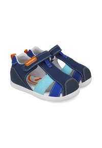 Sandalias de lona marinas con acentos en azul y turquesa, que cuentan con correas de Velcro y una suela de goma blanca. Logo distintivo en el lateral.