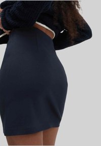 Gonna mini nera, aderente, realizzata in tessuto liscia, con vita alta e design minimalista senza chiusure o decorazioni visibili.