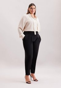 Flødefarvet bluse med prikker og knappelukning samt sorte, skræddersyede bukser med høj talje. Modellen har sorte sandaler med hæl på; glatte, strukturerede stoffer.