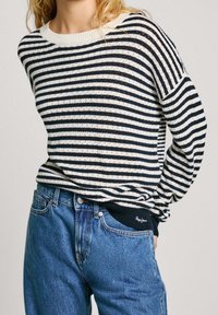 Marinblå och vit randig stickad tröja med ribbad rund halsringning och långa ärmar, i kombination med högmidjade blå denimjeans.