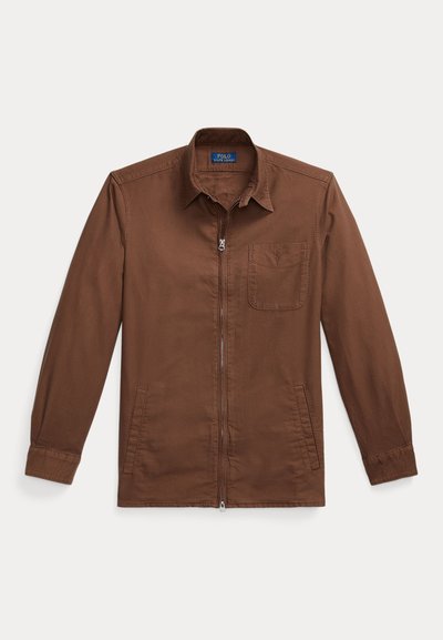 Ruda zip-up striukė, pagaminta iš audinio, su smailiu apykakle, viena krūtinės kišenė ir mygtukinėmis rankovėmis. Minimalistinis ir funkcionalus dizainas.